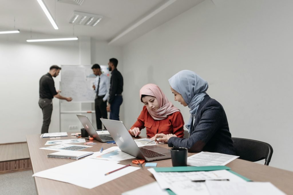 Two women in hijabs and colleagues collaborate on a project in a modern office environment.